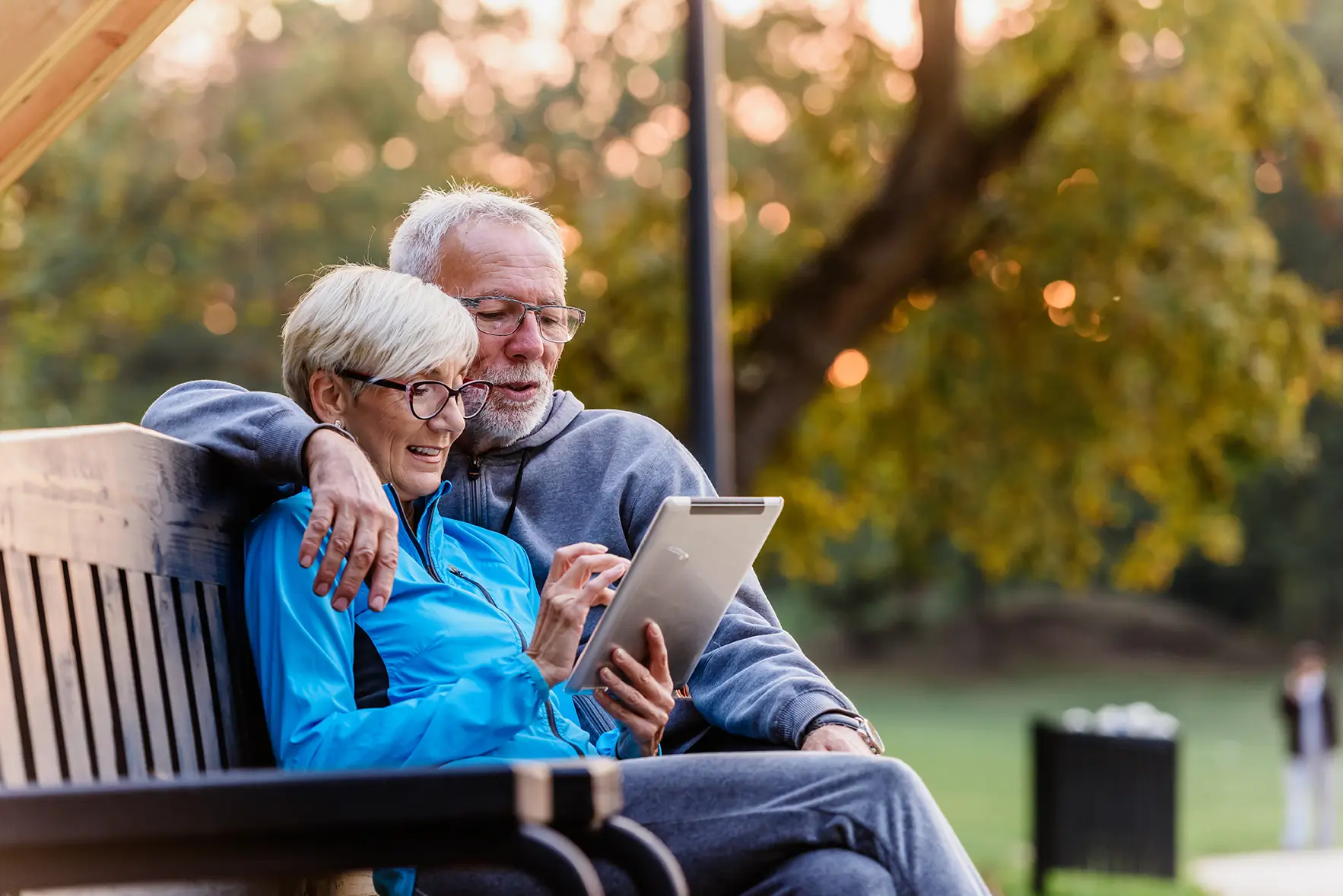 Senior couple using tablet on park bench, planning portfolio management and financial future in Spring, TX.
